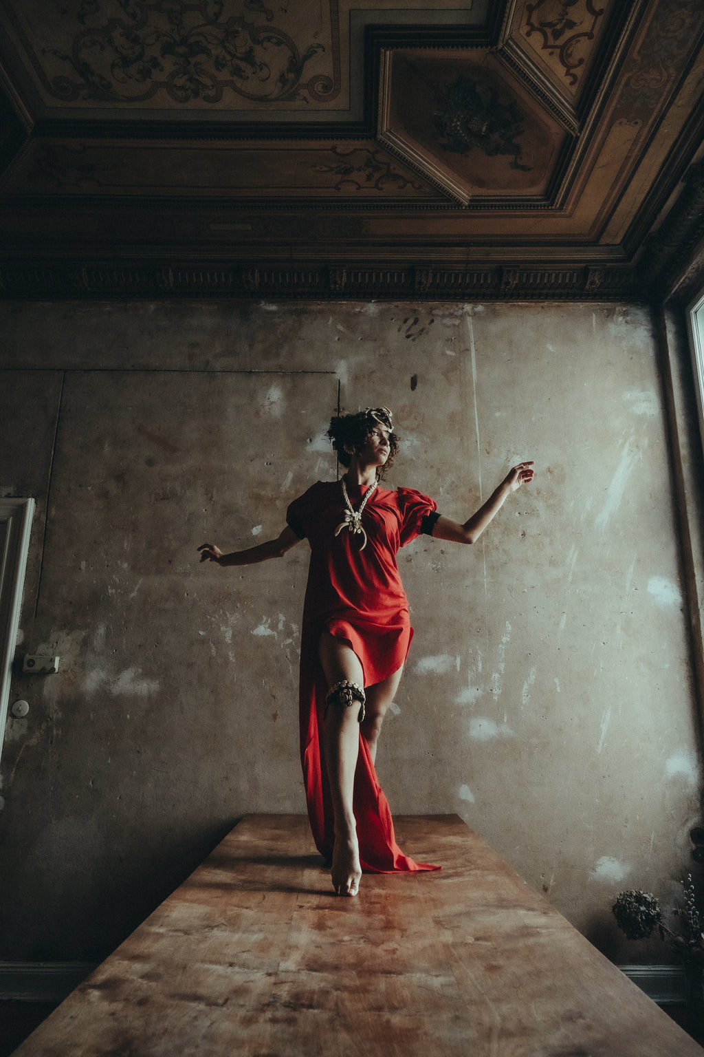 Model wearing the red Sexy Talar beside a window against a textured wall. Photography © 2026 Shannon Kone.