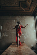 Model wearing the red Sexy Talar beside a window against a textured wall. Photography © 2026 Shannon Kone.