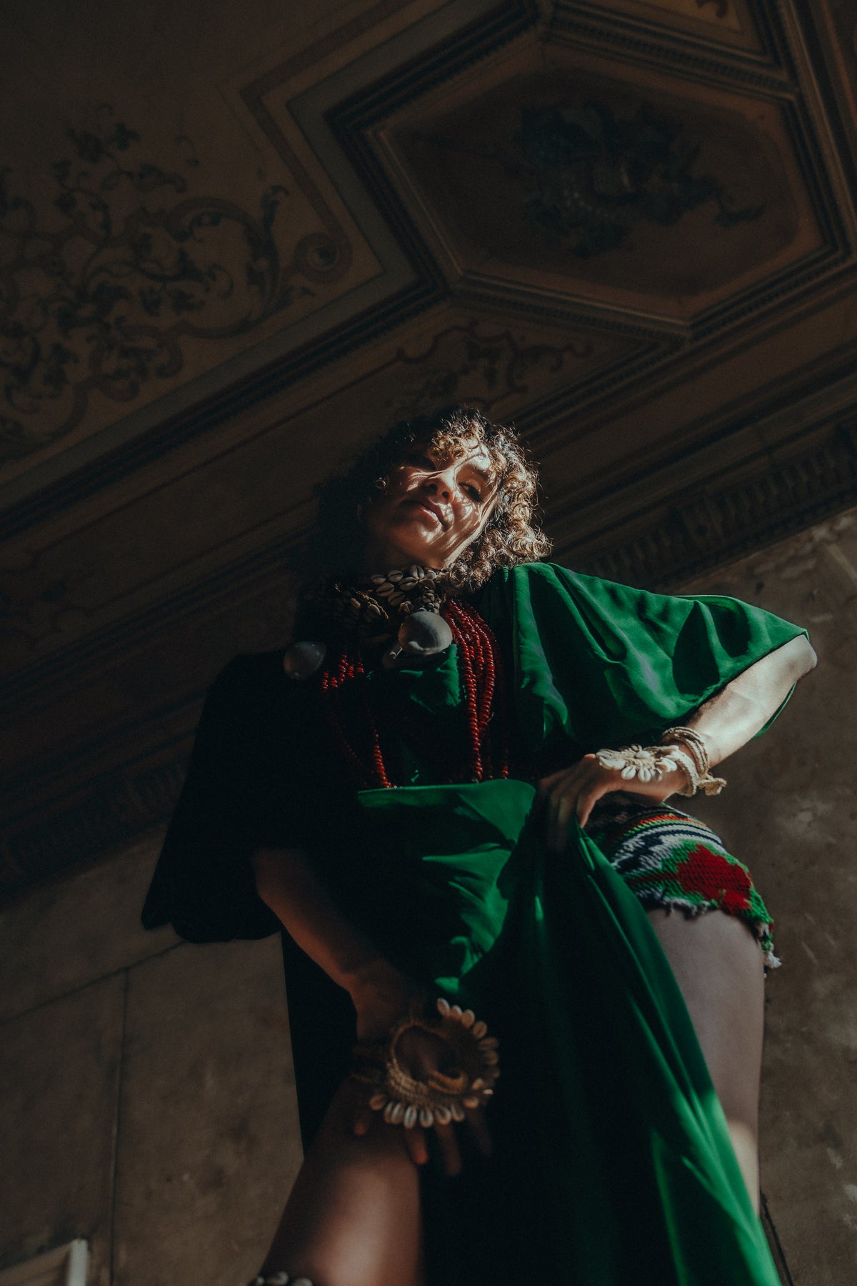 Low-angle portrait of a model wearing a green Sexy Talar with red and shell jewellery.