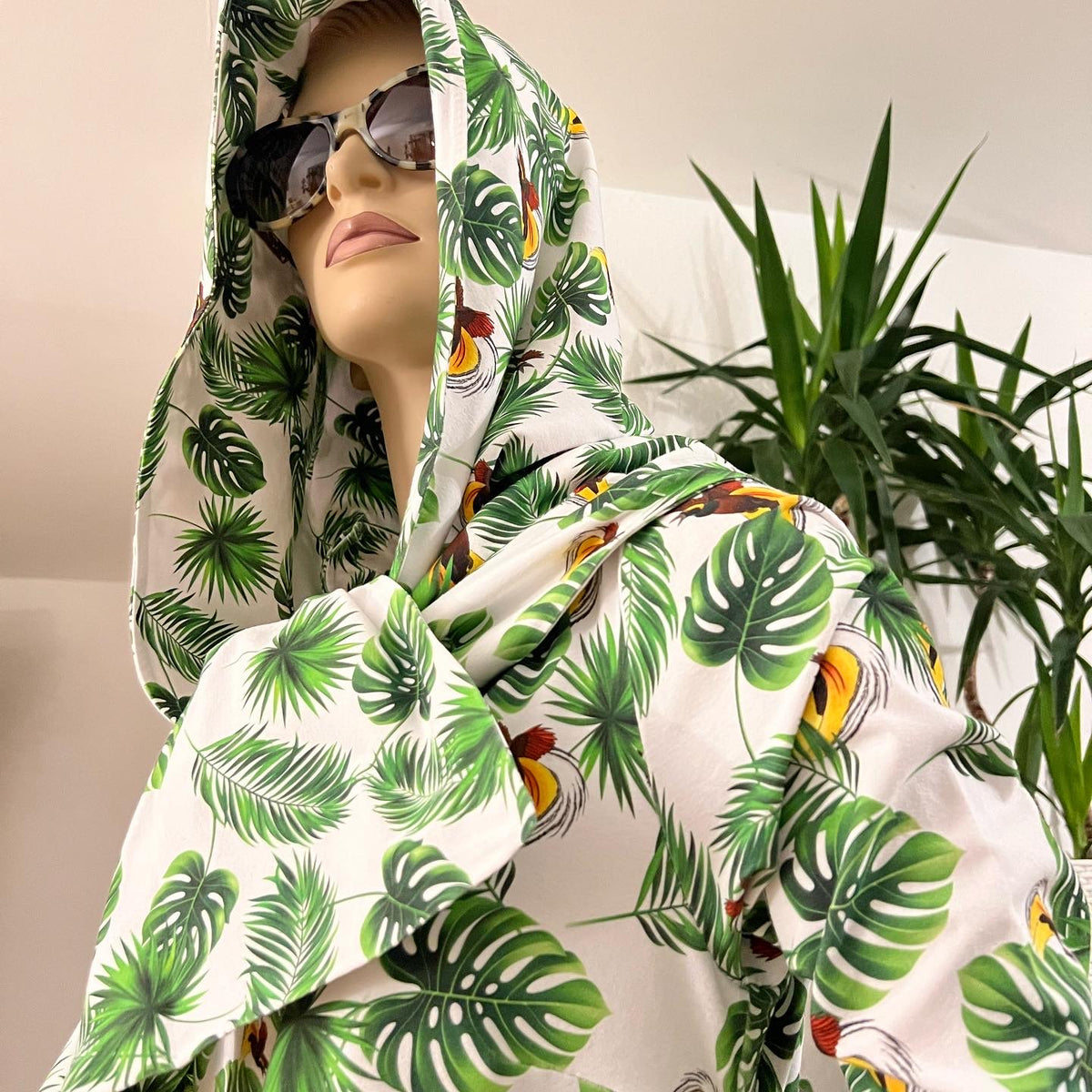 Mannequin draped in white fabric printed with green leaves and colourful birds of paradise.