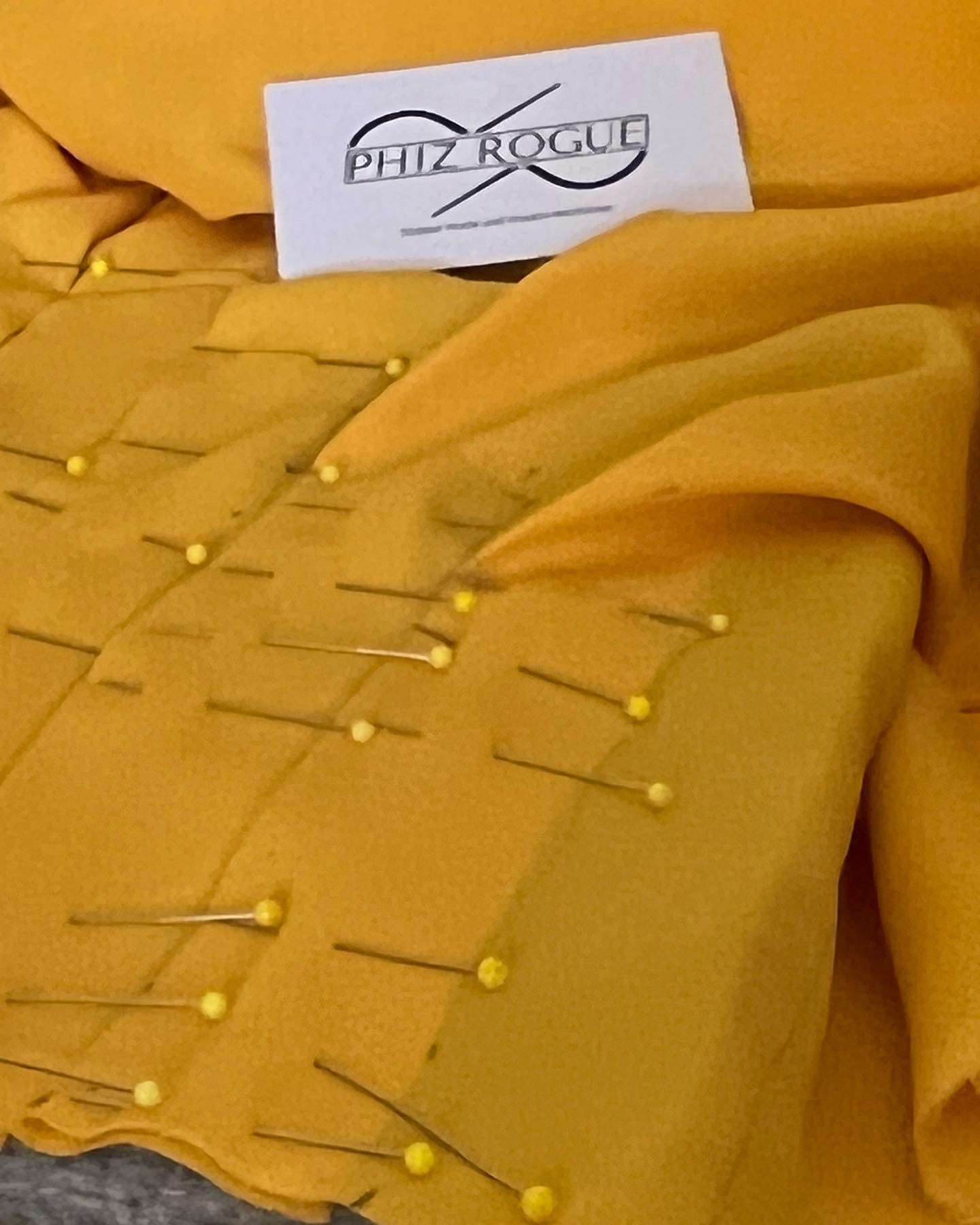 Yellow fabric held with dressmaking pins beside a Phiz Rogue label.